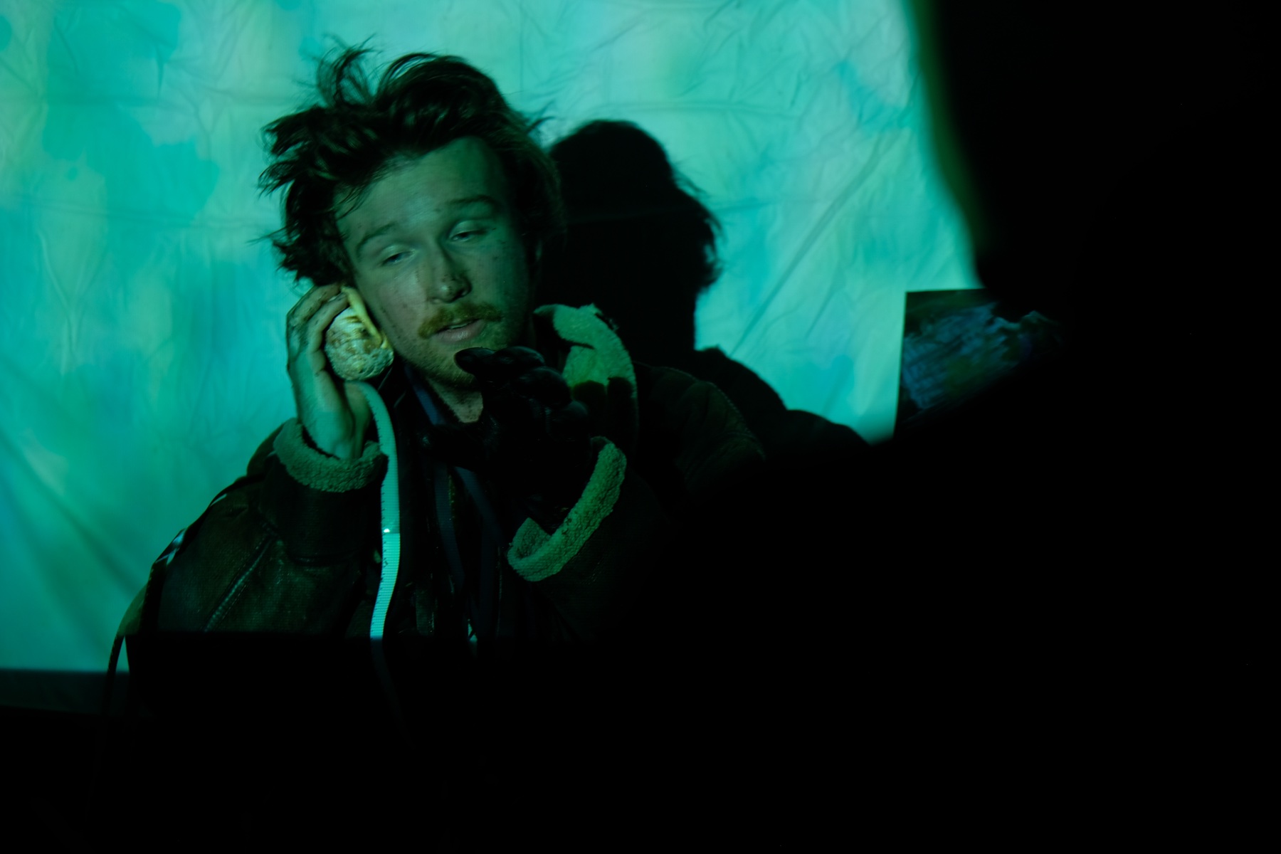 Performer holding a shell to their ear under green projection light.