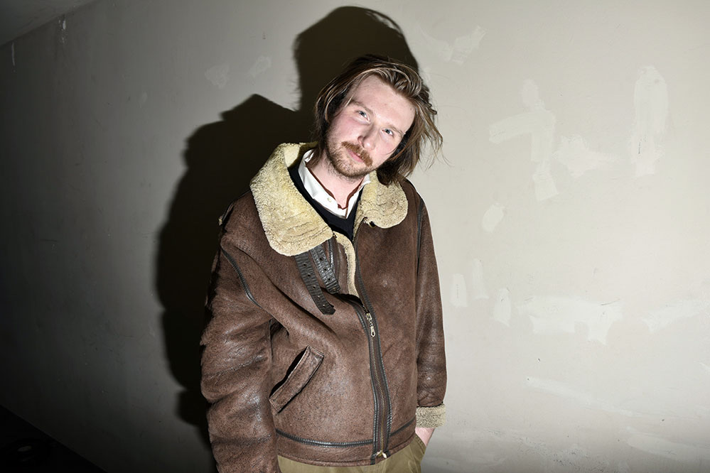 Daniel Zander in a brown shearling jacket against a pale wall.