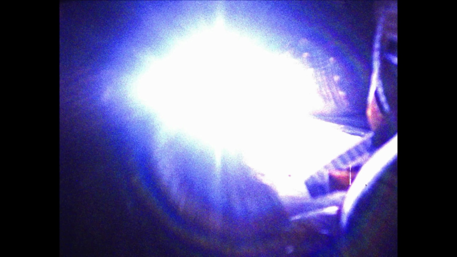 Bright blue flare cutting across a dark performance frame in Skull And Stare Alone.